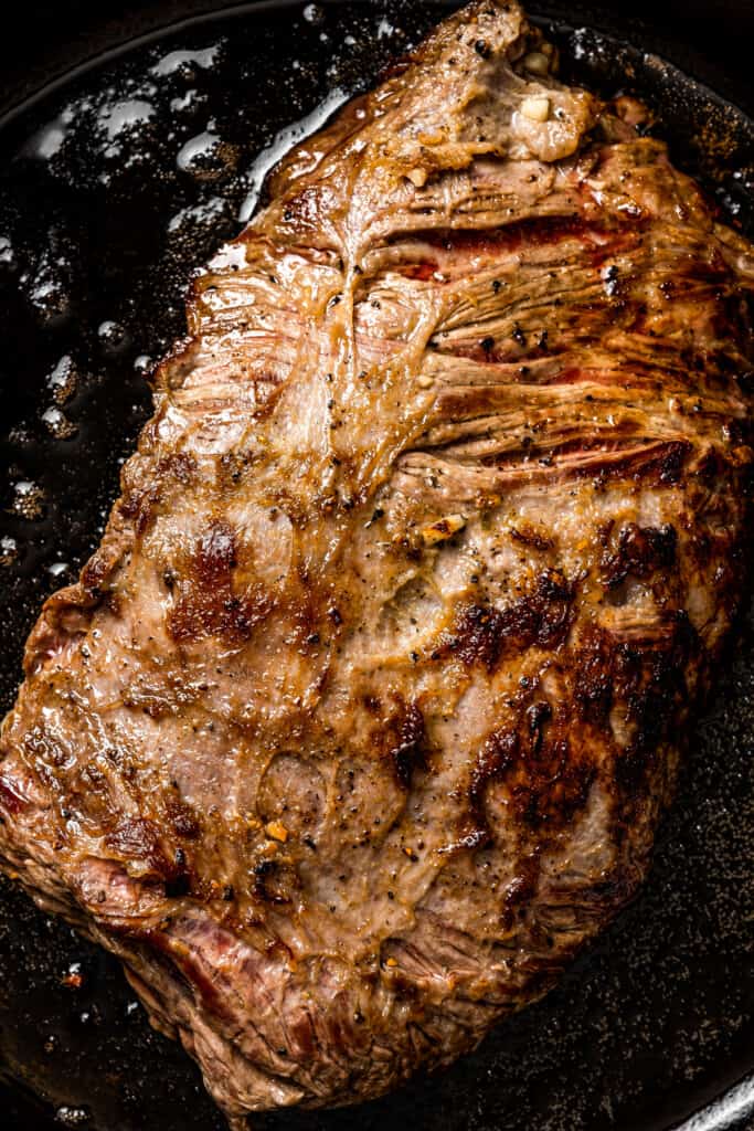 Closeup of searing flank steak in a pan.
