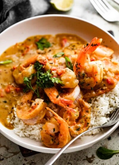 side shot of a bowl with shrimp curry served over white rice, with a fork set inside the bowl.